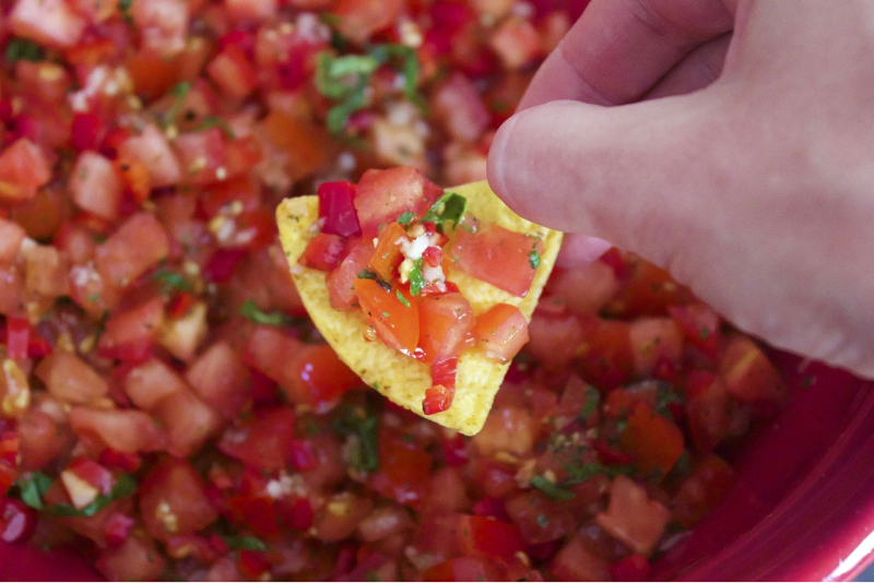 O mână ținând un nacho cu salsa deasupra unui bol de sos