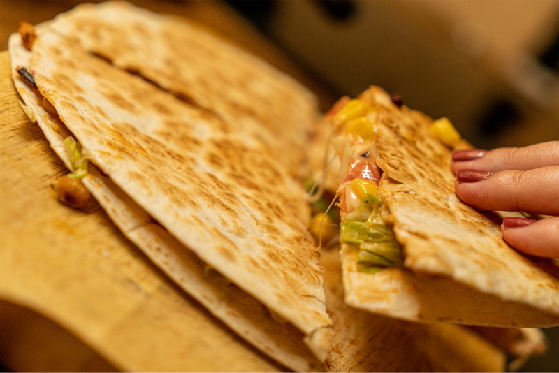 Prim-plan cu o mână ținând o bucată de quesadilla, mâncare mexicană tradițională