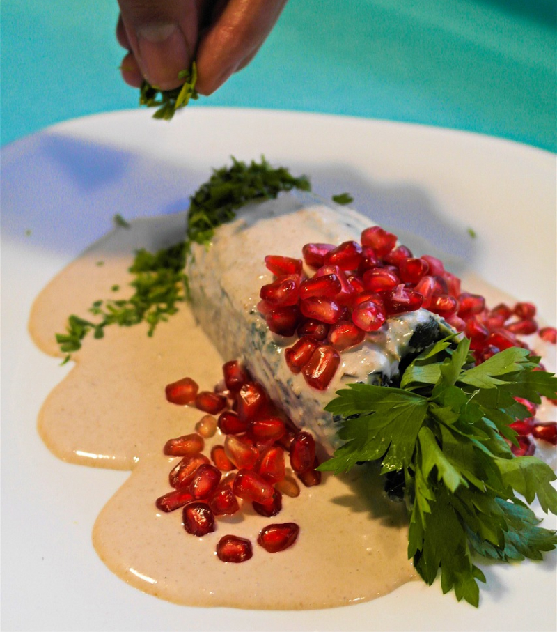 Mână punând pătrunjel peste chiles en nogada, mâncare mexicană tradițională